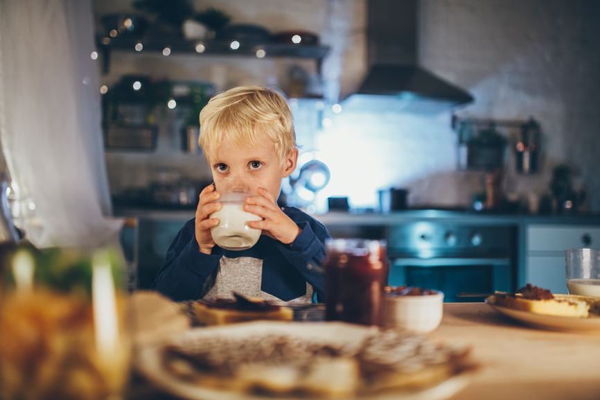 Cute Caucasian little boy having dinner and drinking milk at kitchen on Christmas time.
