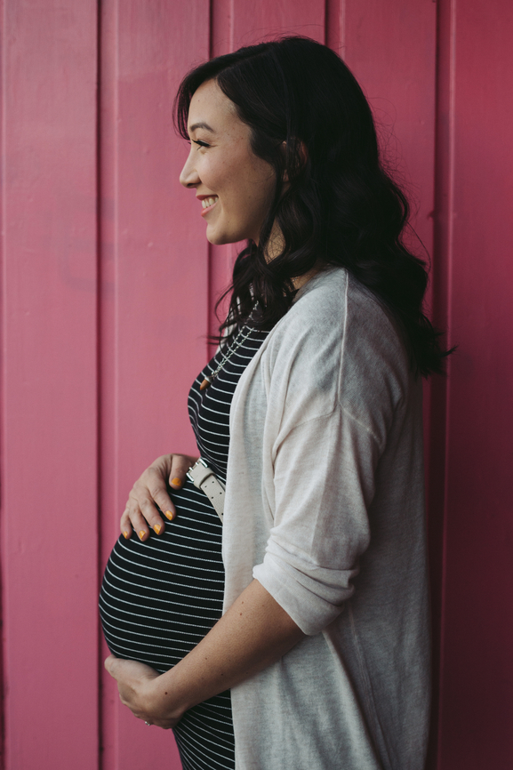 Pretty young pregnant woman standing near pink wall outside