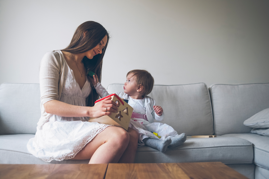 Mother playing with her little girl sitting on the sofa.