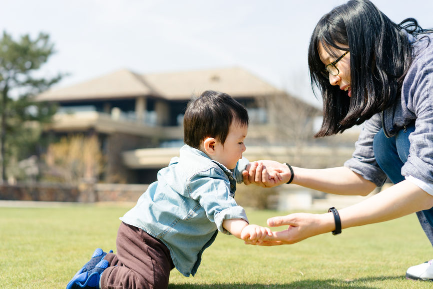 Baby Boy Crawling Towards His Mother On Grass In A Garden